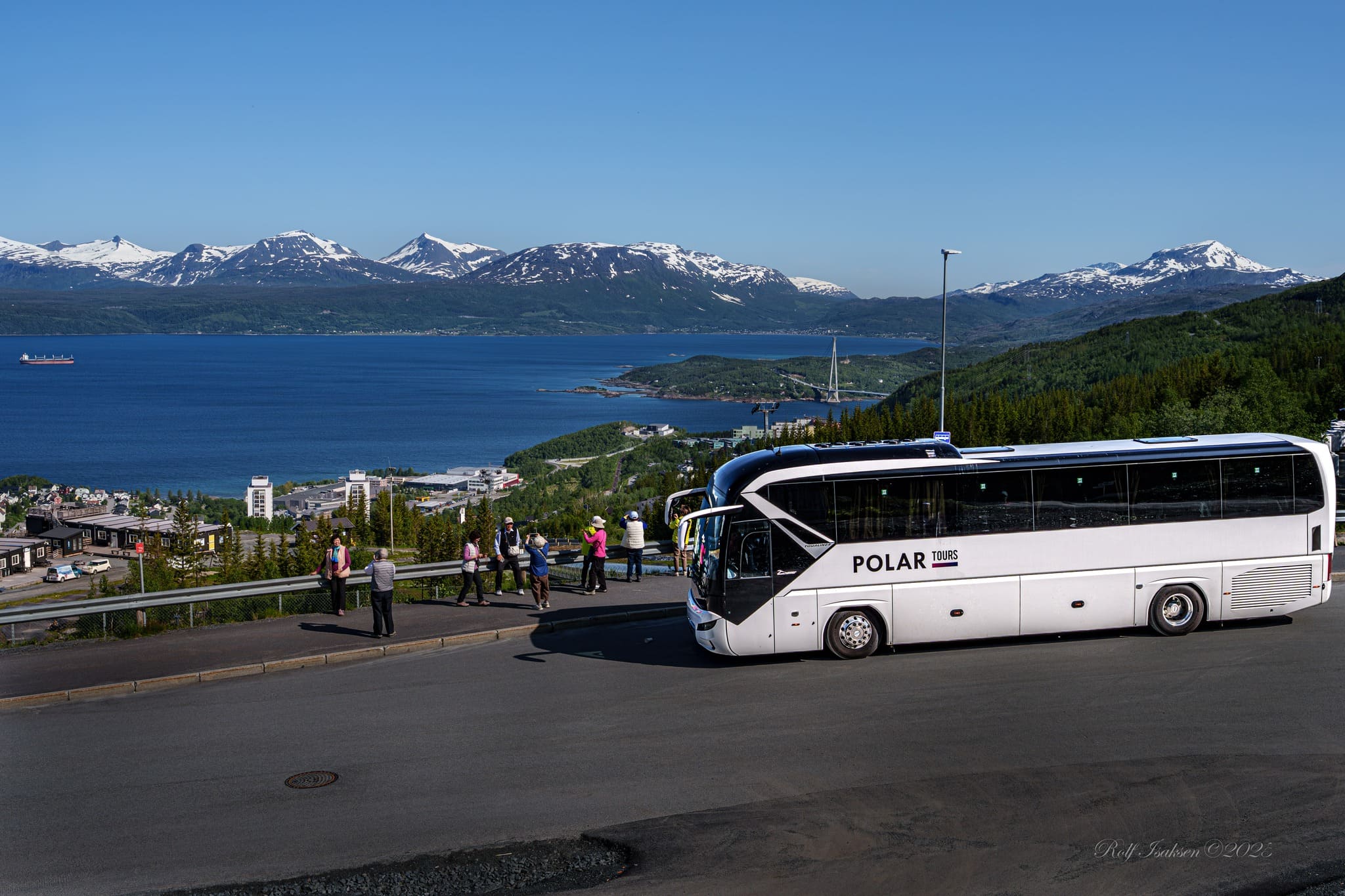Polar Tours sightseeing coach overlooking a Norwegian fjord and snow-capped mountains, fitted with EasyGuide multi-language audio commentary for visitors exploring the Arctic Circle region
